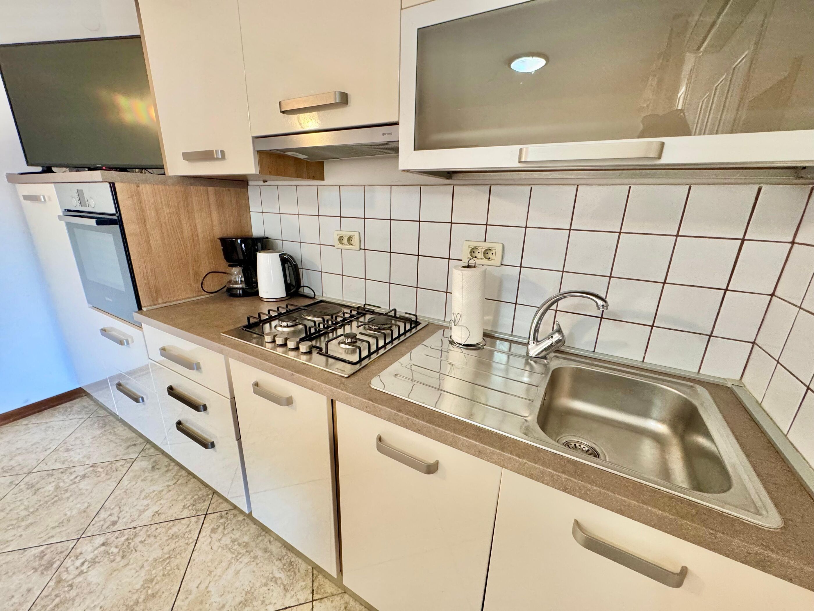 A modern kitchen with a gas stove, a built-in oven, a coffee maker, and a stainless steel sink.