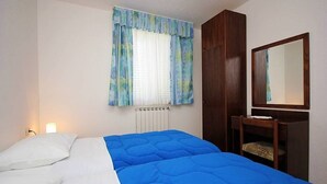 Ein Schlafzimmer mit einem Bett, einem Nachttisch, einem Spiegel und einem Fenster mit Vorhängen.