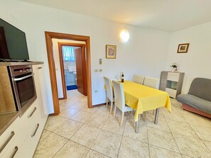 Un coin repas avec une table dressée pour quatre personnes, un canapé, un téléviseur et un espace cuisine équipé d’un four.