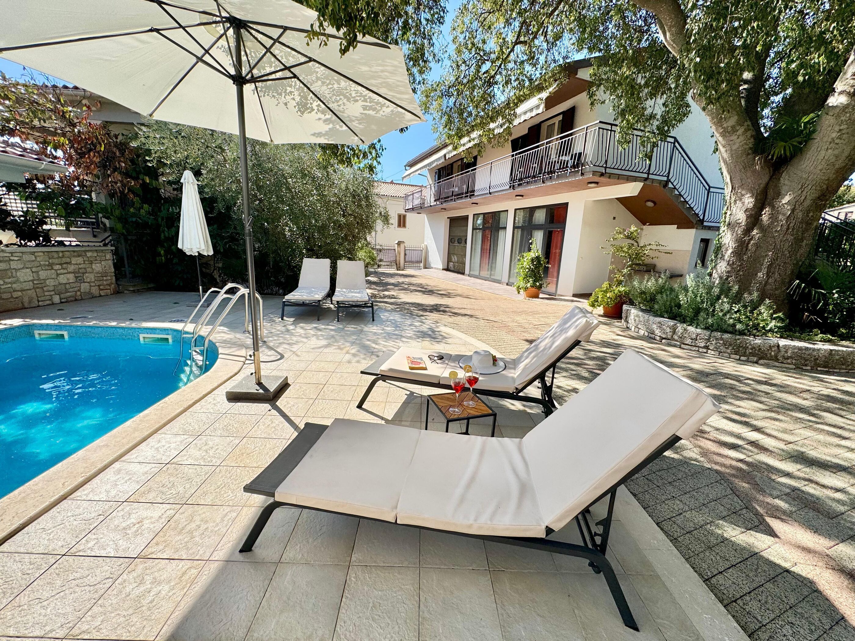 A swimming pool with lounge chairs and a table, surrounded by a stone patio and a building with a balcony.