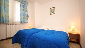 Un dormitorio con dos camas, un radiador, una ventana con cortinas, un cuadro colgado en la pared y lámparas de noche.