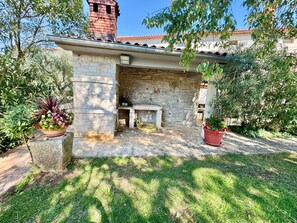 A stone-built outdoor area with a fireplace, surrounded by potted plants and a grassy lawn. - Apartments Ladonia (16296-A3) - Krnica (Pula) (Krnica (Pula))