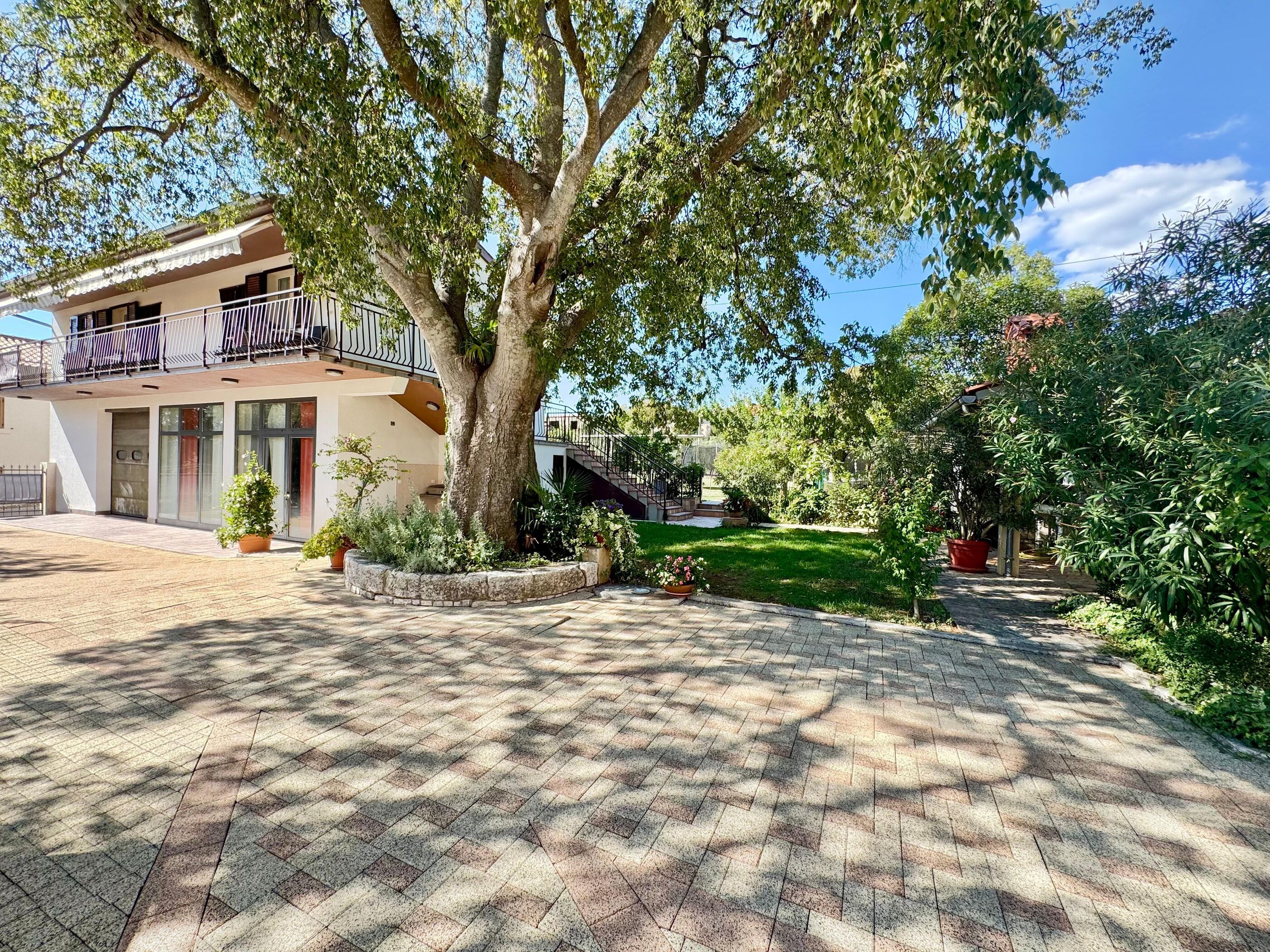 A building with a balcony, a tree in the courtyard, and a paved walkway.