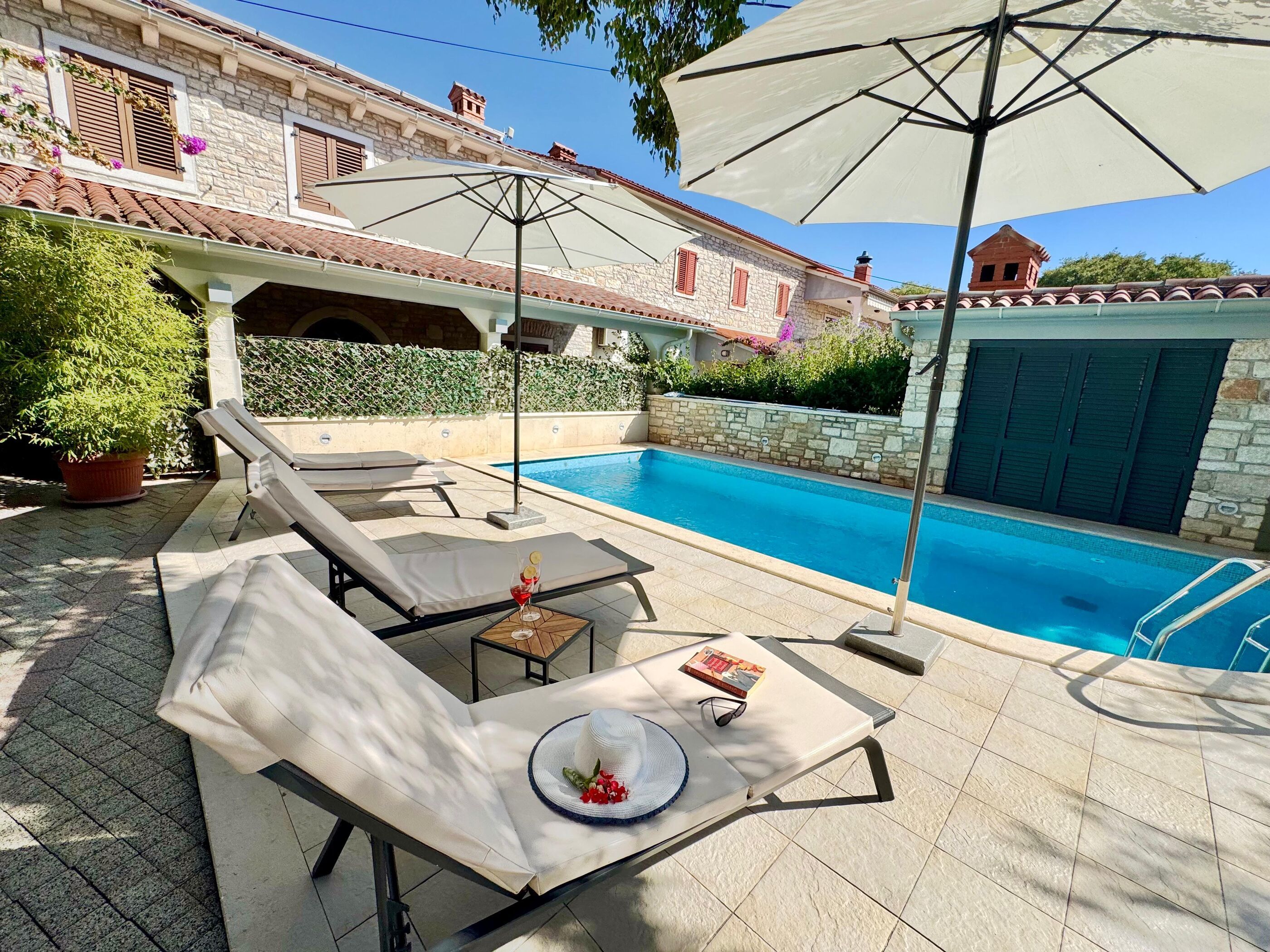Un espace aménagé au bord de la piscine, avec des chaises longues, une table avec des boissons et des parasols.