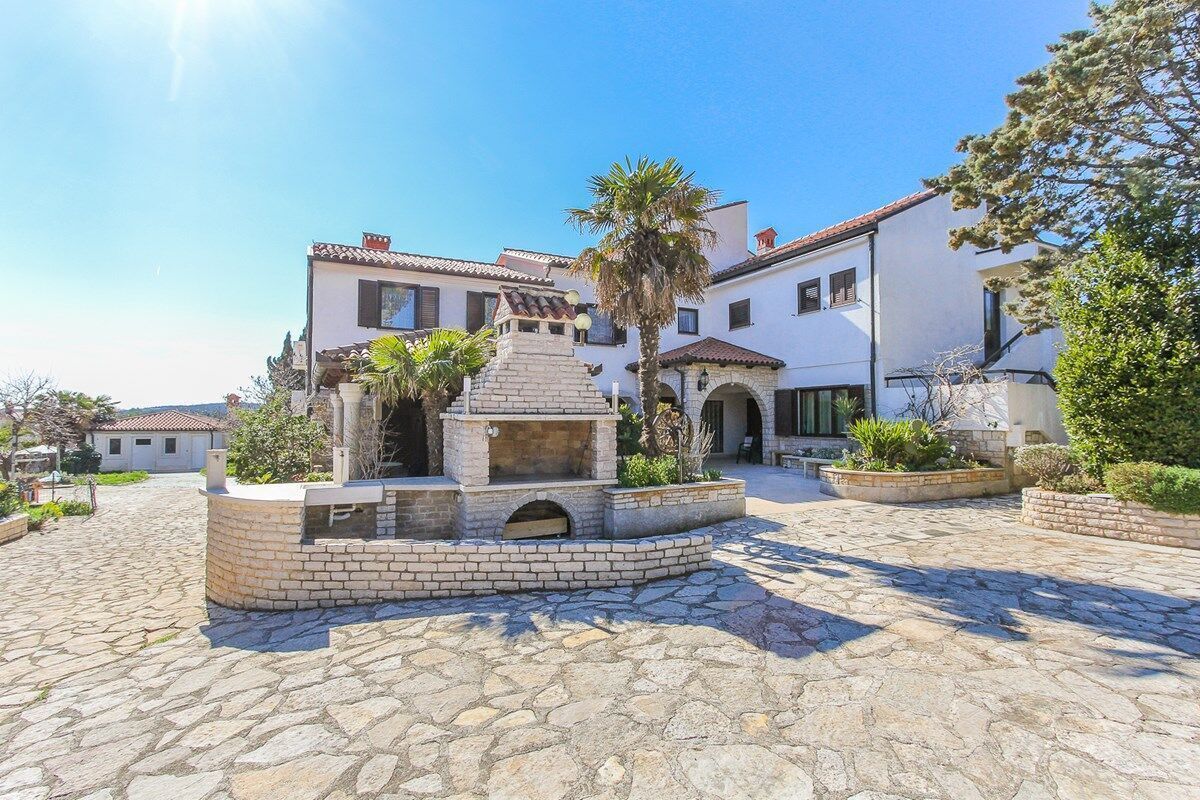 A courtyard with a stone-paved ground, a central stone structure, and surrounding buildings with traditional architecture.