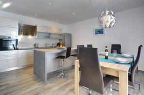A modern kitchen with a central island, bar stools, and a dining table set for two. - House Miceli (16498-K1) - Liznjan (Liznjan)