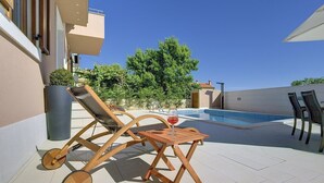 Un espace aménagé au bord de la piscine, avec un fauteuil de relaxation en bois, une petite table et un verre de vin rouge.