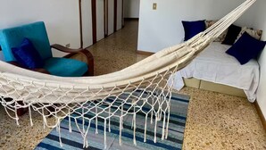 Una hamaca en una habitación con un sillón azul, una cama con almohadones azules y una alfombra a rayas.
