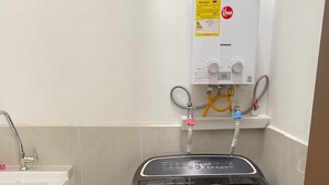 Una habitación pequeña con una lavadora negra, un lavamanos blanco y un calentador de agua en la pared.