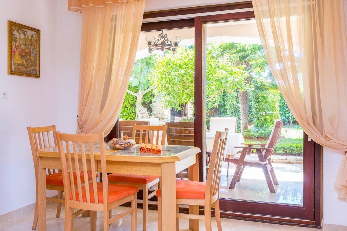 Un espace repas comprenant une table et des chaises, un lustre et une vue sur la verdure environnante.