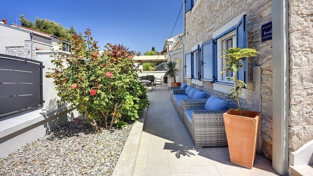 A narrow street with a stone building featuring blue shutters and a sign indicating it is an apartment. There is a small garden with a bush and a potted plant. - Apartments Hodak (16589-A1) - Pula (Pula)
