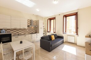 A modern kitchen with a dining area, a sofa, and a window with blinds. - Rental in Rome Vatican Museum Apartment (Rome)