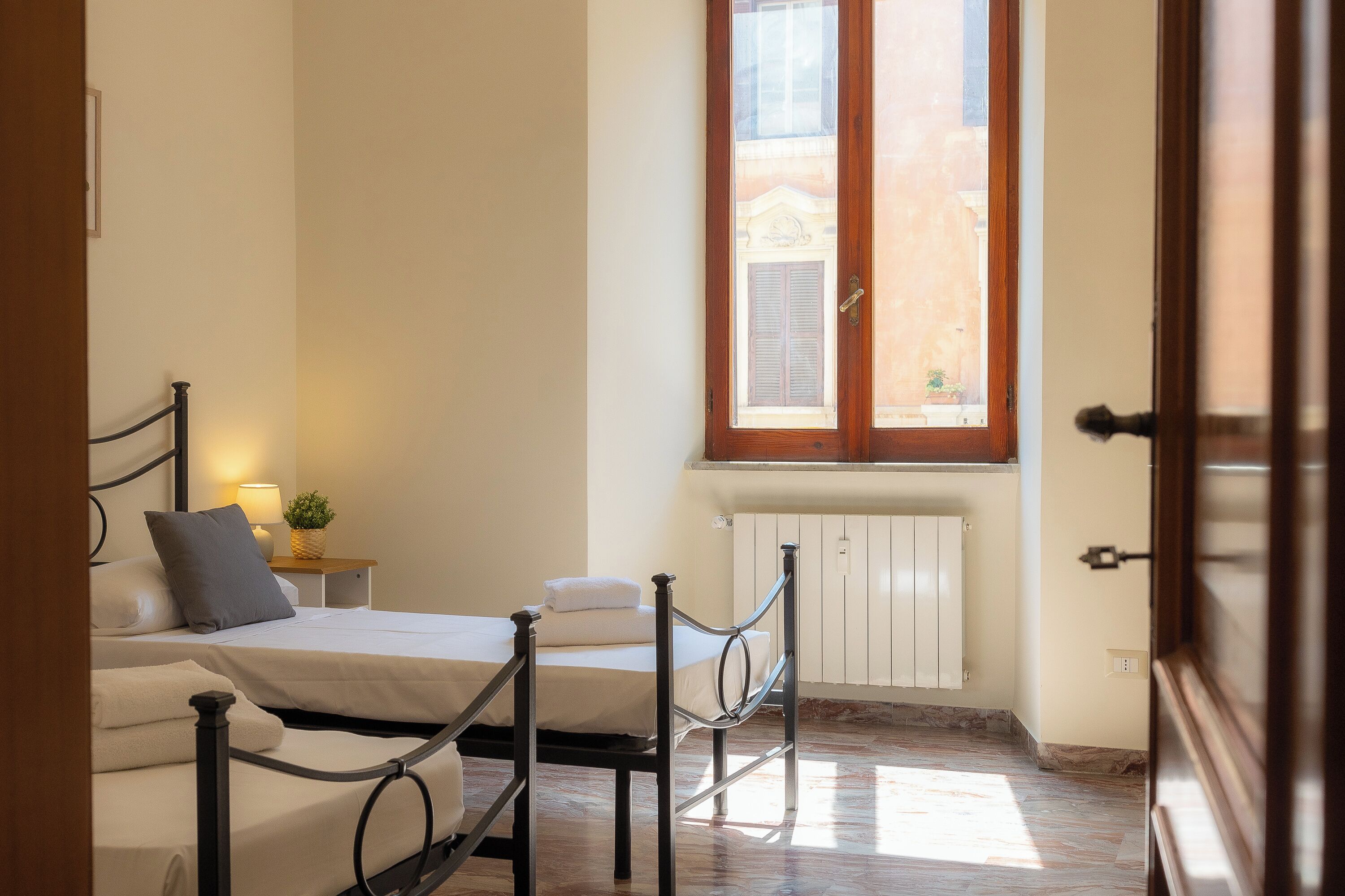 A hotel room with a bed, bedside table, lamp, and a window with shutters.