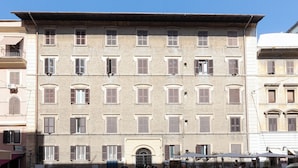 Ein mehrstöckiges Gebäude mit einheitlichem Baustil, das regelmäßig angeordnete Fenster und einen zentralen Eingang mit einem dekorativen Bogen aufweist.