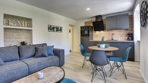Uma sala de estar moderna com um sofá cinza, uma mesa de centro e uma área de jantar com cadeiras azuis e uma mesa de madeira.