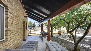 Un patio techado con dos zonas de estar acolchadas, un muro de ladrillo y vista a la calle.