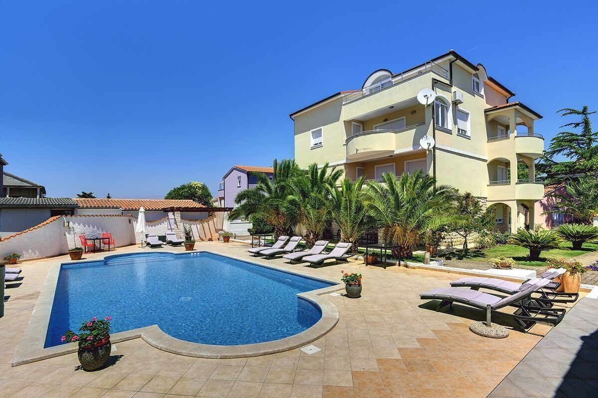 A swimming pool with lounge chairs and a building with balconies.