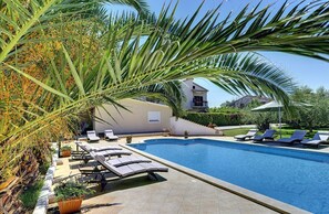 Ein Swimmingpool mit Liegestühlen, umgeben von Palmen und einem Haus im Hintergrund.