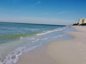 Ein Strand mit blauem Himmel, sanften Wellen und einem Gebäude in der Ferne.