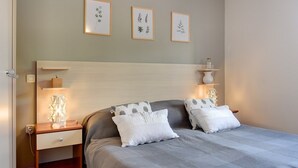 Una camera da letto con un letto, due comodini, un tavolino, una lampada e tre stampe botaniche incorniciate appese al muro.
