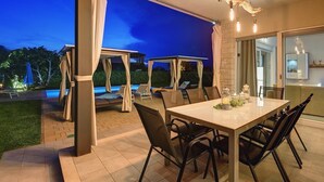 Een buiten eethoek met een tafel en stoelen, een zwembad op de achtergrond en een overdekt terras.