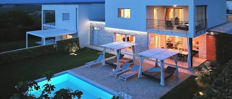 A modern two-story house with a swimming pool, outdoor seating, and a well-maintained garden.