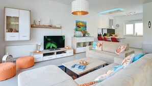 Een moderne woonkamer met een televisie, bank, poef en een decoratieve hanglamp.