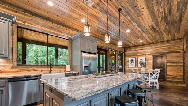 A modern kitchen with granite countertops, stainless steel appliances, and a large island with bar stools. - Riverstone Estate | Luxe Creekside Group Getaway (Hochatown)