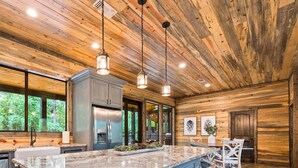 A modern kitchen with wooden walls, a large island, stainless steel appliances, and pendant lighting. - Riverstone Estate | Luxe Creekside Group Getaway (Hochatown)