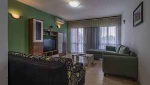 Un salon avec un canapé vert, un téléviseur, une petite table et une fenêtre avec des rideaux.