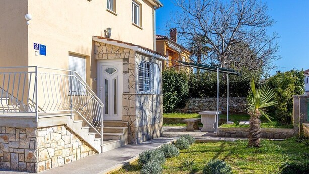 Un edificio con escalones de piedra que llevan a una puerta, un pequeño jardín con una palmera y un cielo azul despejado.