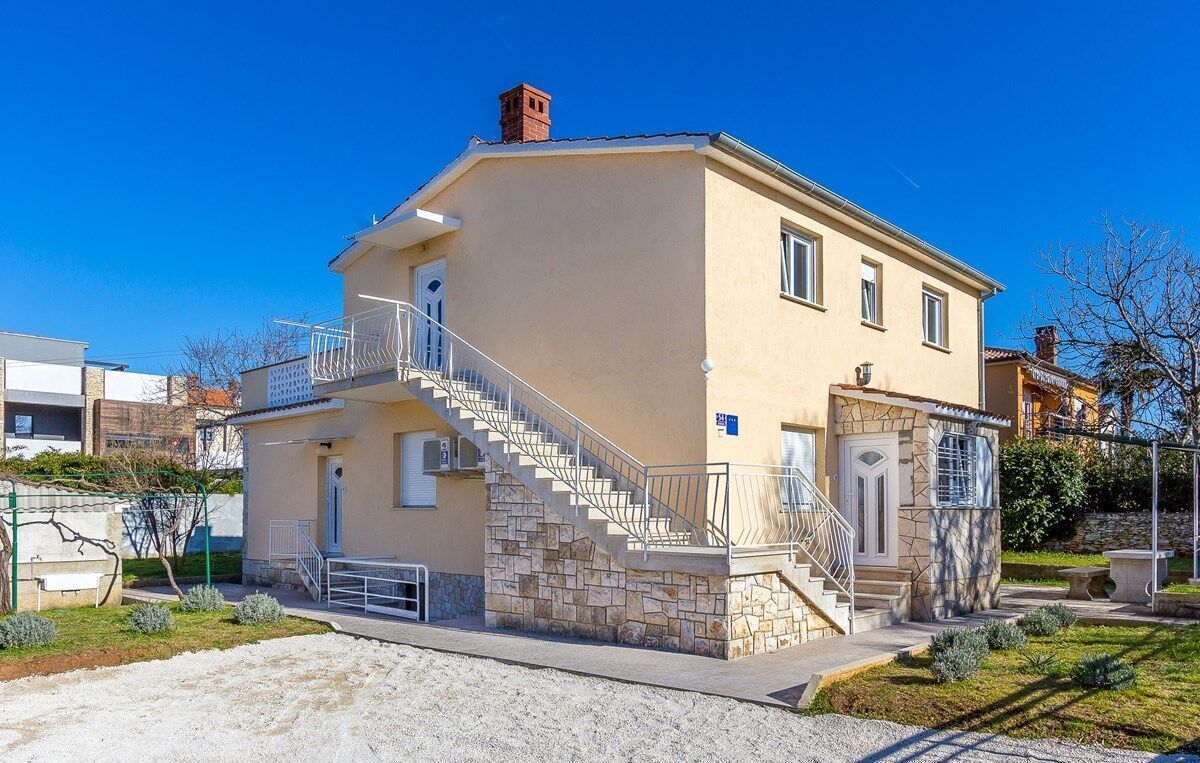 Un edificio de dos pisos con fachada de piedra, una escalera que lleva a la entrada y un pequeño jardín.