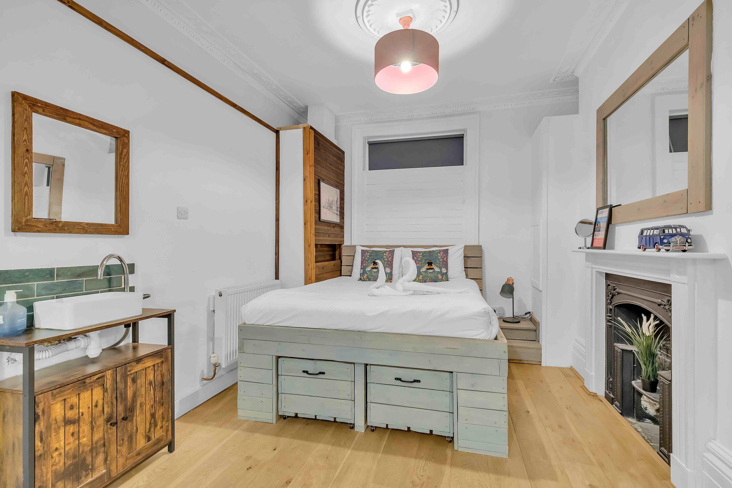 A bedroom with a wooden bed, a white radiator, a wooden cabinet, a mirror, and a fireplace.