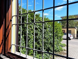 A window with metal bars, a view of a white car parked outside, and a building with a yellow facade in the background. - Apartment with private parking just a 10-minute walk from the historic center (Lucca)