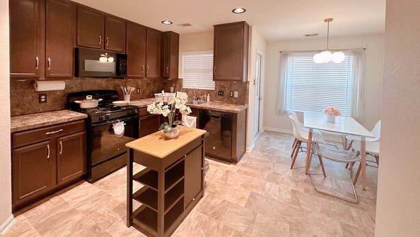 A kitchen with dark wooden cabinets, a granite countertop, a stove, and a dining area with a white table and chairs. - Clean & Calm 3BR Home Near Houston Premium Outlets (Cypress)