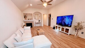 A modern living room with a sectional sofa, a flat-screen TV, wooden flooring, and a ceiling fan. - Clean & Calm 3BR Home Near Houston Premium Outlets (Cypress)