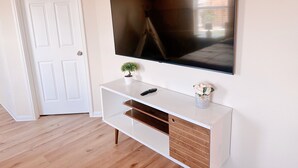 A room with a white door, a mounted TV on a white console, a small potted plant, and a remote control. - Clean & Calm 3BR Home Near Houston Premium Outlets (Cypress)
