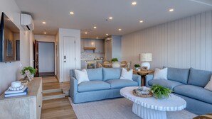 Una sala moderna con un sofá azul, una mesa de centro blanca y una cocina al fondo.