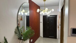 A hallway with a modern chandelier, a wooden slat wall, a black door, and a mirror reflecting the ceiling. - 3 Bedroom En-Suite, Wi-Fi, Secured, 24/7 Power (Lekki)