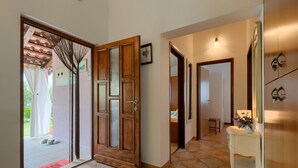 Un couloir avec une porte en bois, une console blanche surmontée d’un vase et un sol carrelé.