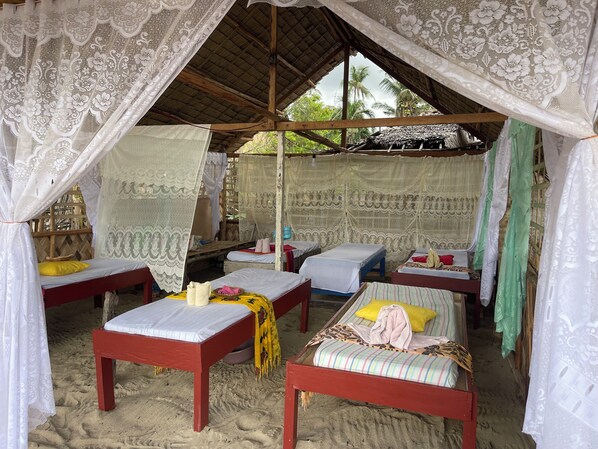 A beach hut with four beds, each with a different colored bedding, and a canopy with lace curtains. - Akoya Beach Park & Cottages (El Nido)