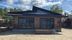 A beachside building with a large glass door, a wooden deck, and a covered seating area. - Akoya Beach Park & Cottages (El Nido)