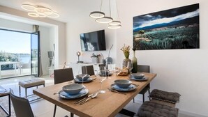 Una zona menjador moderna amb taula de fusta preparada per a sis persones, un televisor de pantalla plana a la paret i un quadre paisatgístic sobre la taula.