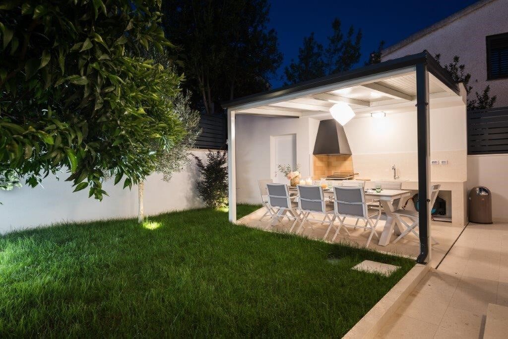 A modern outdoor kitchen with a dining area, surrounded by a well-maintained lawn and a tree.