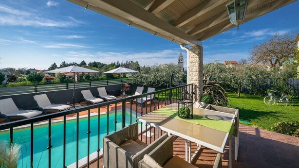 A poolside area with lounge chairs and a table, a clear blue sky, and a distant view of a church tower. - Villa Laura (16946-K1) - Krnica (Pula) (Krnica (Pula))