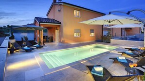 Ett område vid poolen med solstolar och parasoller, en swimmingpool och en byggnad med en satellantenn.