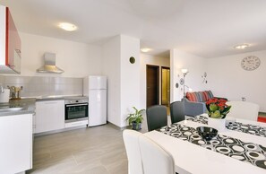 A modern kitchen with white cabinets, a built-in oven, and a refrigerator. There is a dining area with a table and chairs, and a clock on the wall. - Villa Kata (73534-K1) - Krnica (Pula) (Krnica (Pula))