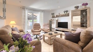 En moderne stue med sofa, lænestole, sofabord og fjernsyn.
