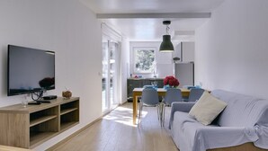 Un soggiorno moderno con televisione a schermo piatto, mobile TV in legno, divano grigio, tavolo da pranzo con sedie e angolo cottura con finestra.
