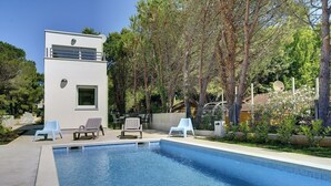 Una piscina con lettini, un edificio moderno e alberi circostanti.